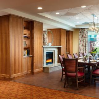 A warmly decorated dining room featuring a wooden table surrounded by chairs, with a fireplace and elegant chandelier.