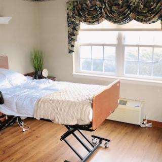 A well-lit hospital room featuring a hospital bed, a plant, and large windows.