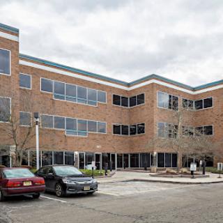 A modern office building featuring large windows and a brick facade, surrounded by a parking area.