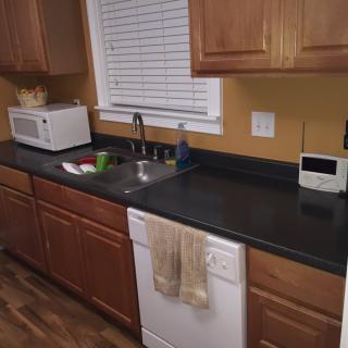 A kitchen with wooden cabinets, a countertop with a microwave, and a sink next to a dishwasher.