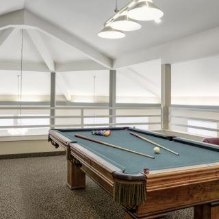 A well-lit game room featuring a pool table with cues and balls ready for play.