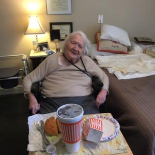 An elderly person enjoying a meal, smiling comfortably in their living space.