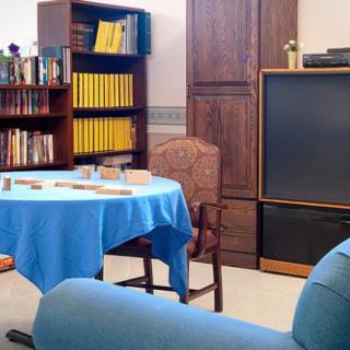 A vintage-style living room with a large television, bookshelf, and a small table covered with a blue tablecloth.