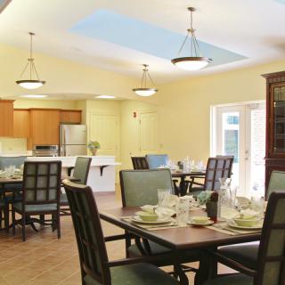 A cozy dining area with neatly set tables and chairs, adjacent to an open kitchen space.