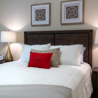 A neatly arranged bedroom with a comfortable bed, accented by a red pillow and flanked by lamps on either side.