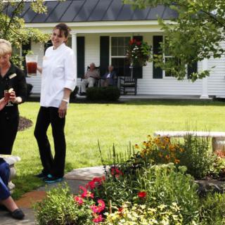 A group of people enjoying a conversation in a garden setting outside a house.