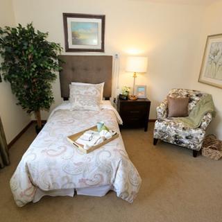 A cozy bedroom with a single bed, lamp, chair, and decorative elements.