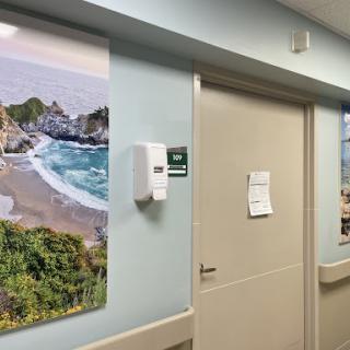 A serene beach landscape adorns the wall of a hospital corridor, providing calming decor in a healthcare setting.