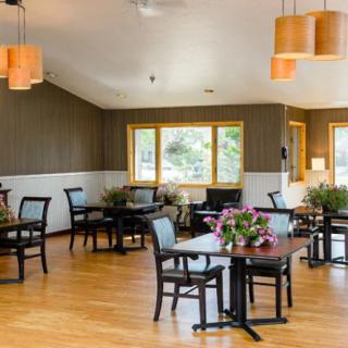 A cozy dining area with neatly arranged tables and chairs, featuring warm lighting and large windows.