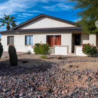 A single-story house with a desert landscape featuring cacti and rocks under a clear blue sky.