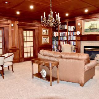 A cozy living room with wooden paneling, featuring a library corner and fireplace.