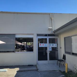 Entrance of a building with visible windows and a chair outside on a sunny day.
