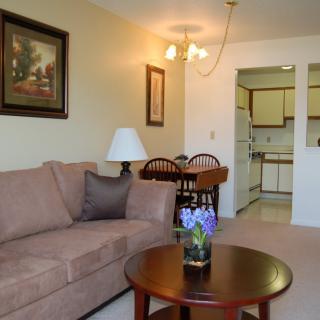A cozy living room with a beige sofa and a wooden coffee table adorned with flowers, leading into a dining area and kitchen.