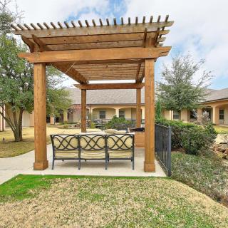 A wooden pergola with outdoor seating in a landscaped garden setting.