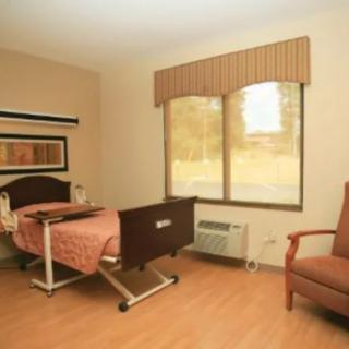 A clean and tidy hospital room with a bed, chair, and large window.