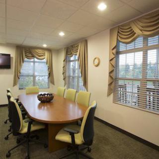 A well-lit conference room with a long table and chairs, featuring large windows with curtains.