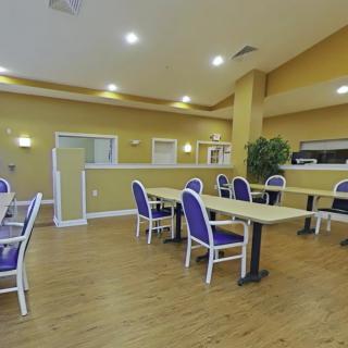 A spacious dining area with wooden flooring, featuring multiple tables and chairs under bright lighting.