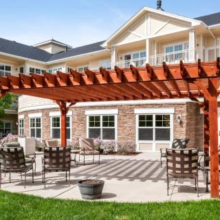 A sunny outdoor patio area with a pergola, surrounded by garden chairs and adjacent to a building.