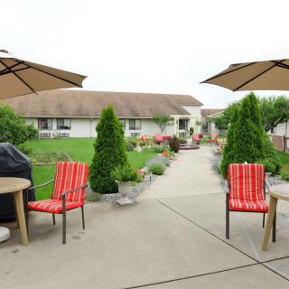 A well-maintained patio with red chairs, umbrellas, and lush greenery in a garden setting.