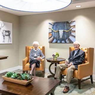 An elderly couple sitting in a modern living room adorned with artwork and decor.