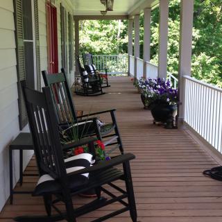 A cozy porch with black rocking chairs and potted plants along a wooden deck.