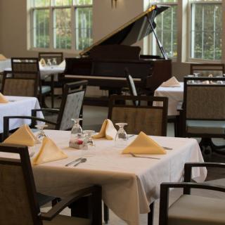 An elegant restaurant interior with neatly set tables and a grand piano in the background.