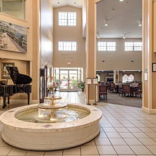 A spacious lobby featuring a central fountain and a grand piano with high ceilings and large windows.