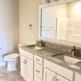 A modern bathroom featuring double sinks with granite countertops and white cabinetry.