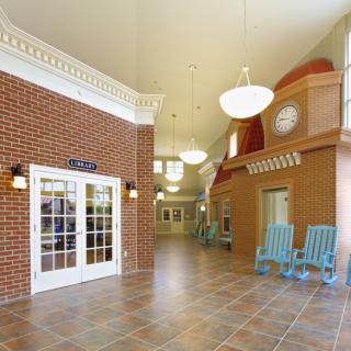 A spacious lobby area with brick walls, tile flooring, and blue rocking chairs.
