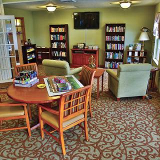 A cozy living room with comfortable seating, a television, and bookshelves filled with books. There is a table with puzzles in progress, creating a warm and inviting atmosphere.