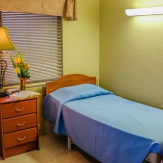 A cozy bedroom with a single bed, nightstand, lamp, and window with curtains.