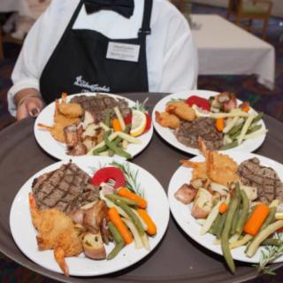 A waiter carrying a tray with plates of steak and mixed vegetables.