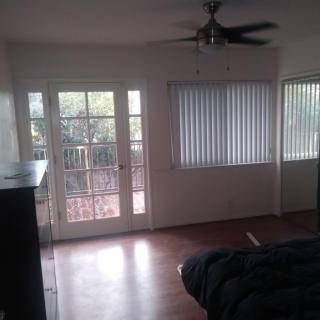 A cozy living room featuring a ceiling fan, large windows with blinds, and a door leading to an outdoor area.