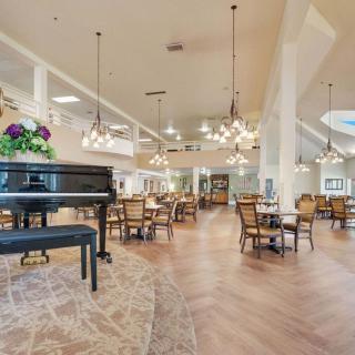 A spacious and elegant dining area featuring a grand piano, decorative chandeliers, and neatly arranged tables and chairs.
