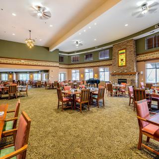 A spacious dining area with multiple tables and chairs, featuring a central fireplace and large windows.