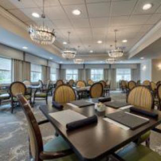 An elegant dining room with neatly arranged tables and chairs, adorned with chandeliers and large windows.