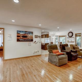A spacious living room with hardwood floors, featuring recliner chairs and artwork on the walls, illuminated by natural light.