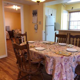 A cozy dining area with a table set for four, adjacent to a kitchen with wooden flooring.