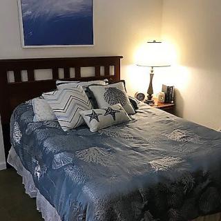 A cozy bedroom with a neatly made bed, decorative pillows, and a bedside lamp.