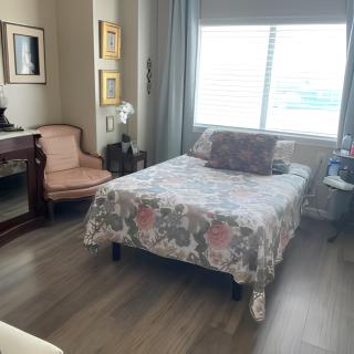 A cozy bedroom with a floral bedspread, chair, and desk by the window.
