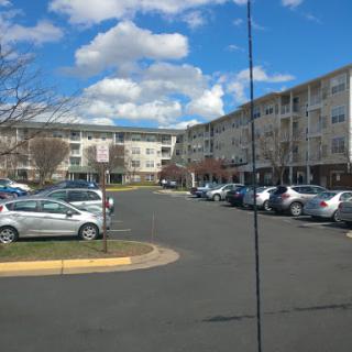A view of a residential apartment complex with cars parked in the lot under a partly cloudy sky.