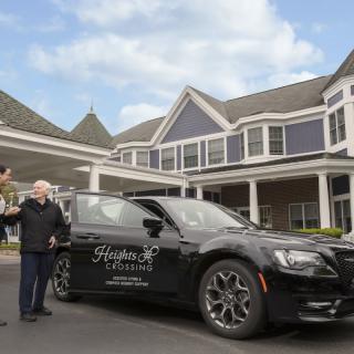 Two people standing next to a luxury car in front of a large building.