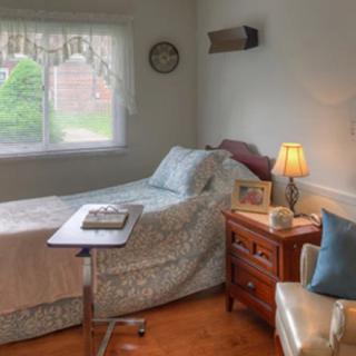 A cozy bedroom with a single bed, bedside table, and lamp next to a window overlooking greenery.