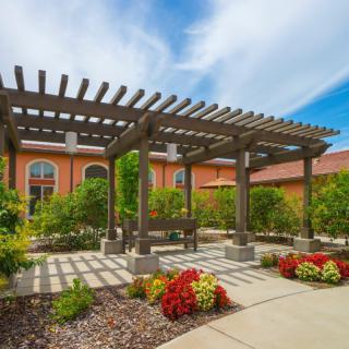 A beautifully designed pergola in a garden setting with colorful flowers and a paved pathway.
