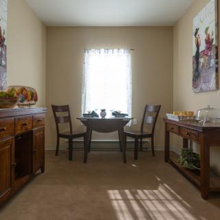 A cozy dining room with a wooden table and chairs, decorated with wall art and illuminated by natural light through a window.