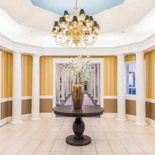 An elegant lobby featuring a stylish chandelier, decorative columns, and a central table with a vase.