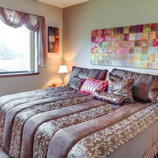 A cozy bedroom featuring a large, patterned bed with pillows, an artwork on the wall, and a window with drapes.