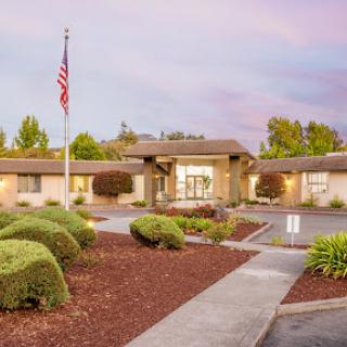 A welcoming entrance to a building surrounded by well-maintained landscaping and an American flag.