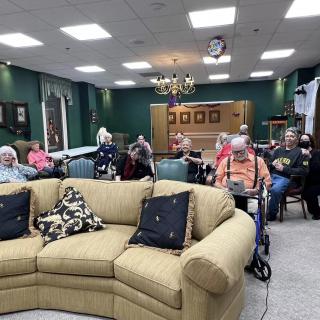 A group of elderly people gathered in a community living room setting, enjoying a social activity.