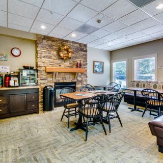 A cozy dining area with tables and chairs, featuring a stone fireplace and warm decor.
